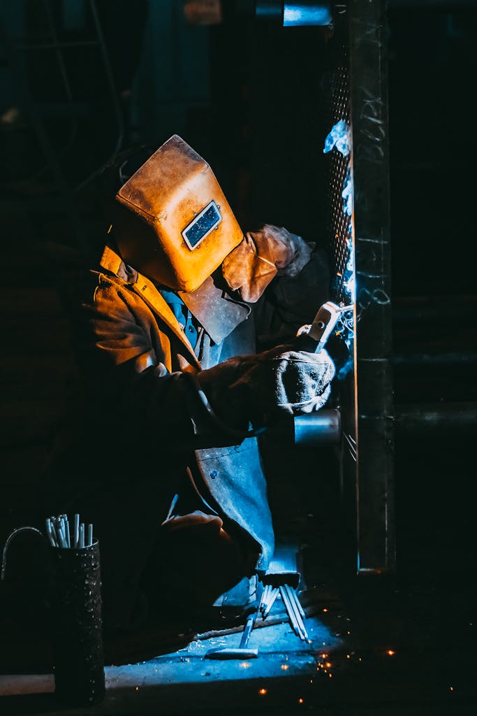 A welder wearing safety gear sparks metal in a dimly lit industrial setting.